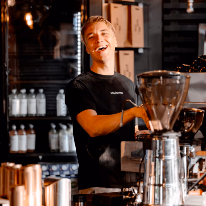 Smiling barista in black shirt preparing coffee behind a café counter with coffee equipment.