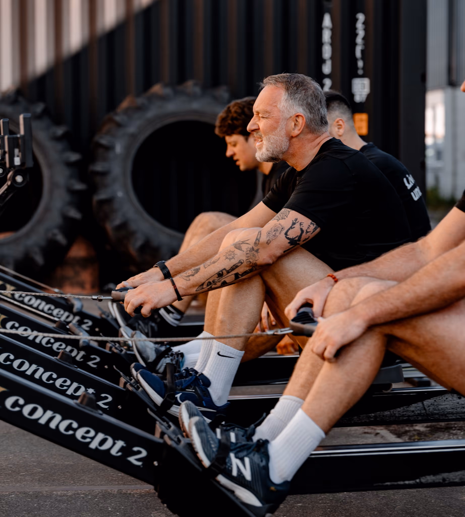 Group of men rowing on Concept2 rowing machines during an outdoor workout.