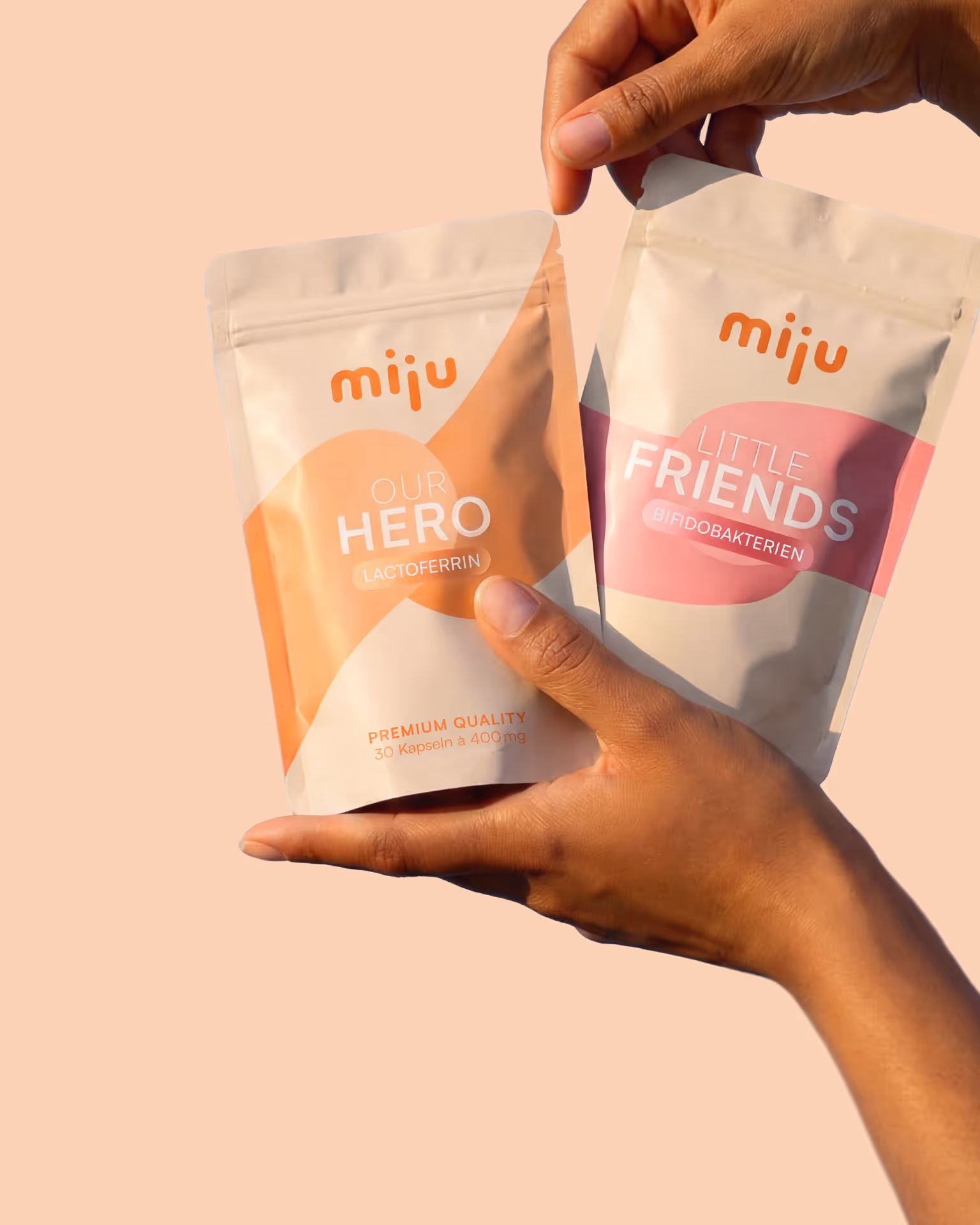 Zwei Hände halten zwei Miju Nahrungsergänzungsmittelverpackungen, eine orange für Lactoferin und eine rosa für Bifidobakterien.