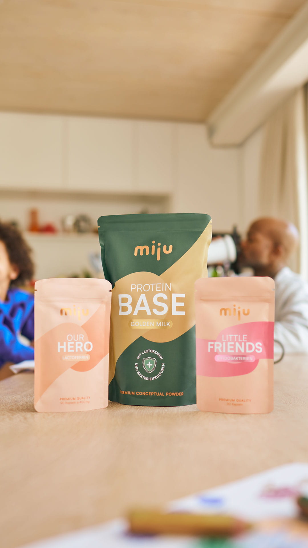 miju Lactoferrin, Bifidobakterien und Proteinpulver vor einer Familie im Alltag. Im Hintergrund trinkt ein Vater einen Proteinshake, während eine Großmutter gemeinsam mit ihrem Enkel lacht.