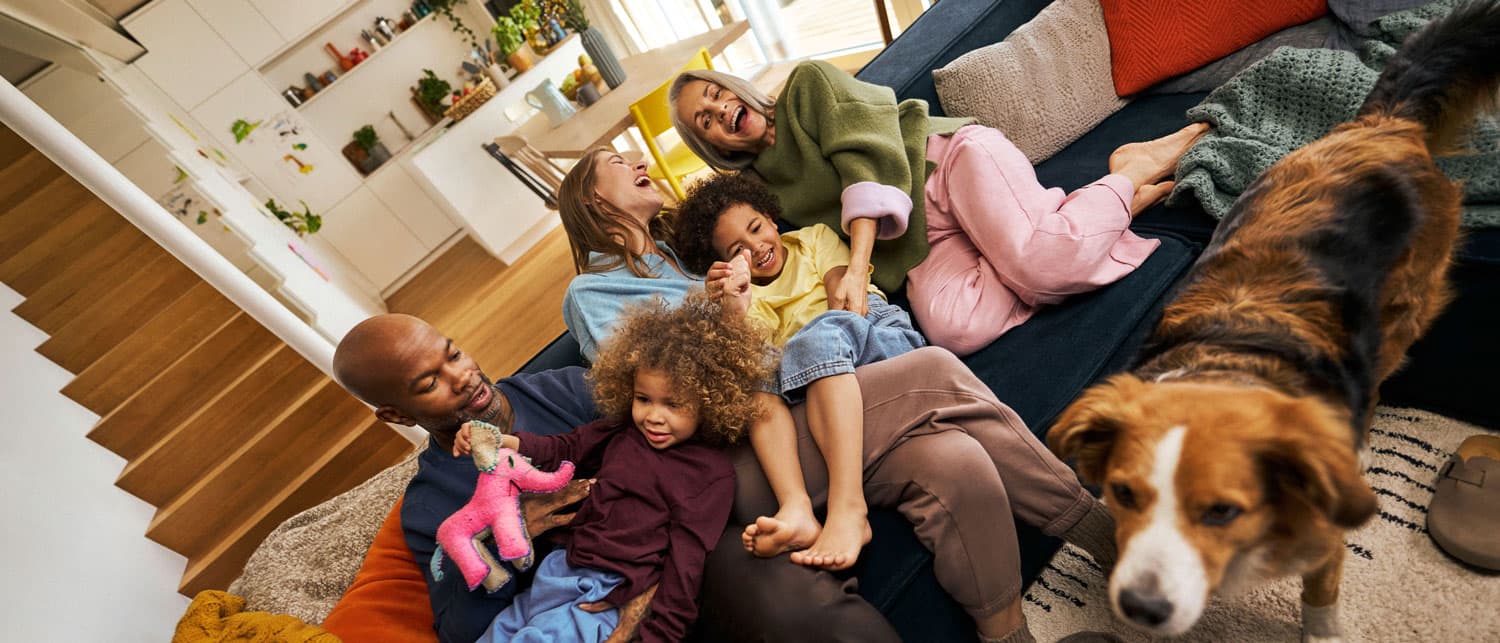 Die ganze Familie verbringt einen unbeschwerten Moment auf der Couch: lachen, spielen, kitzeln und kuscheln gemeinsam mit ihrem Hund. Die Szene vermittelt Freude, Zusammenhalt und wertvolle Familienzeit.