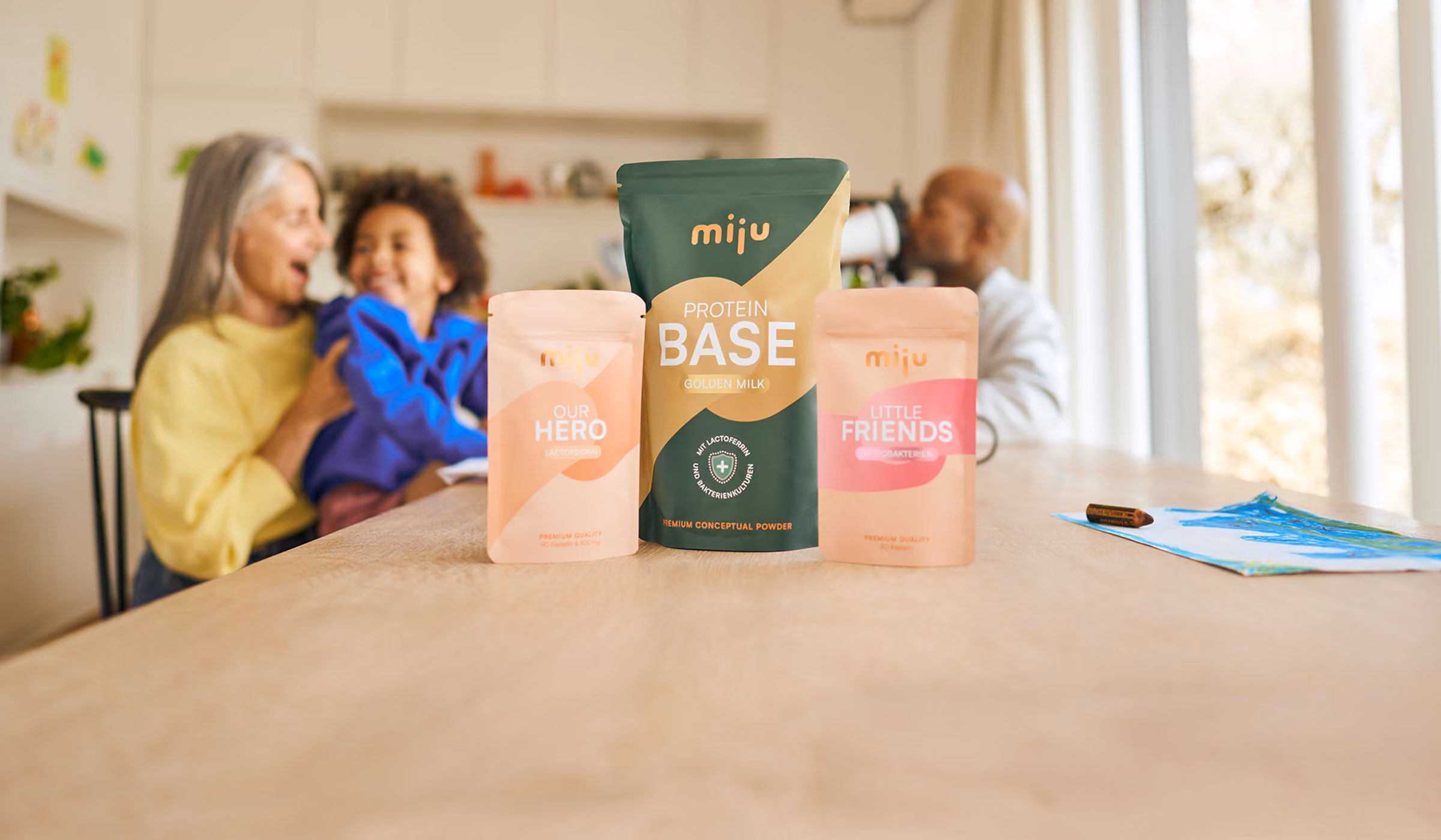 miju Lactoferrin, Bifidobakterien und Proteinpulver vor einer Familie im Alltag. Im Hintergrund trinkt ein Vater einen Proteinshake, während eine Großmutter gemeinsam mit ihrem Enkel lacht.