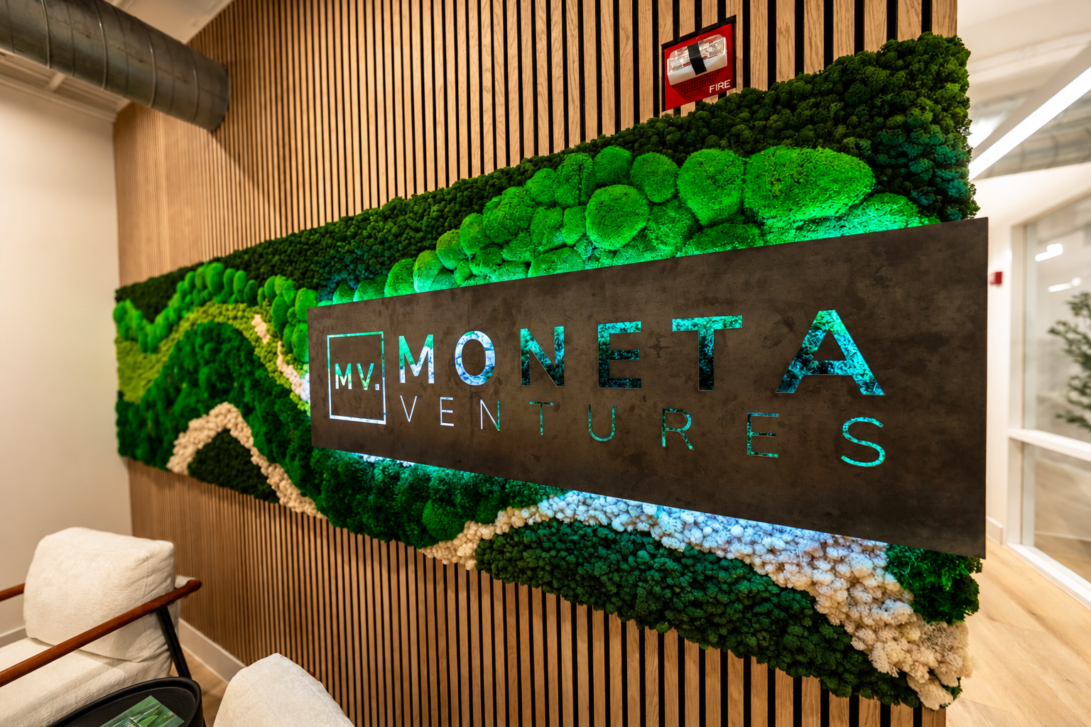 Preserved moss feature wall on wood slat backing with a backlit Moneta Ventures logo in a corporate office lounge