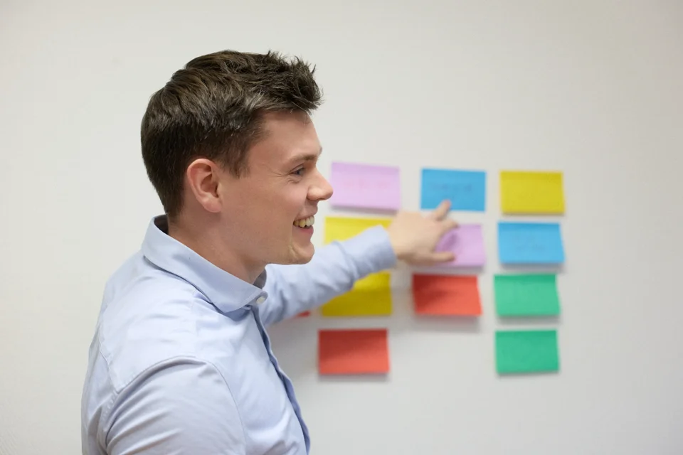 Two men discussing and writing on a whiteboard with orange and blue markers in an office setting.
