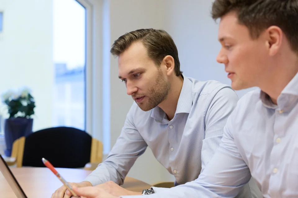 Smiling man in a dark sweater holding a marker and engaging with another person in a light blue shirt.