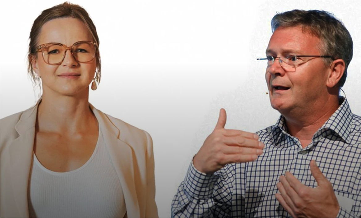 Eine Frau mit Brille und hellbeiger Jacke lächelt, während ein Mann mit kariertem Hemd und Brille gestikuliert und spricht.