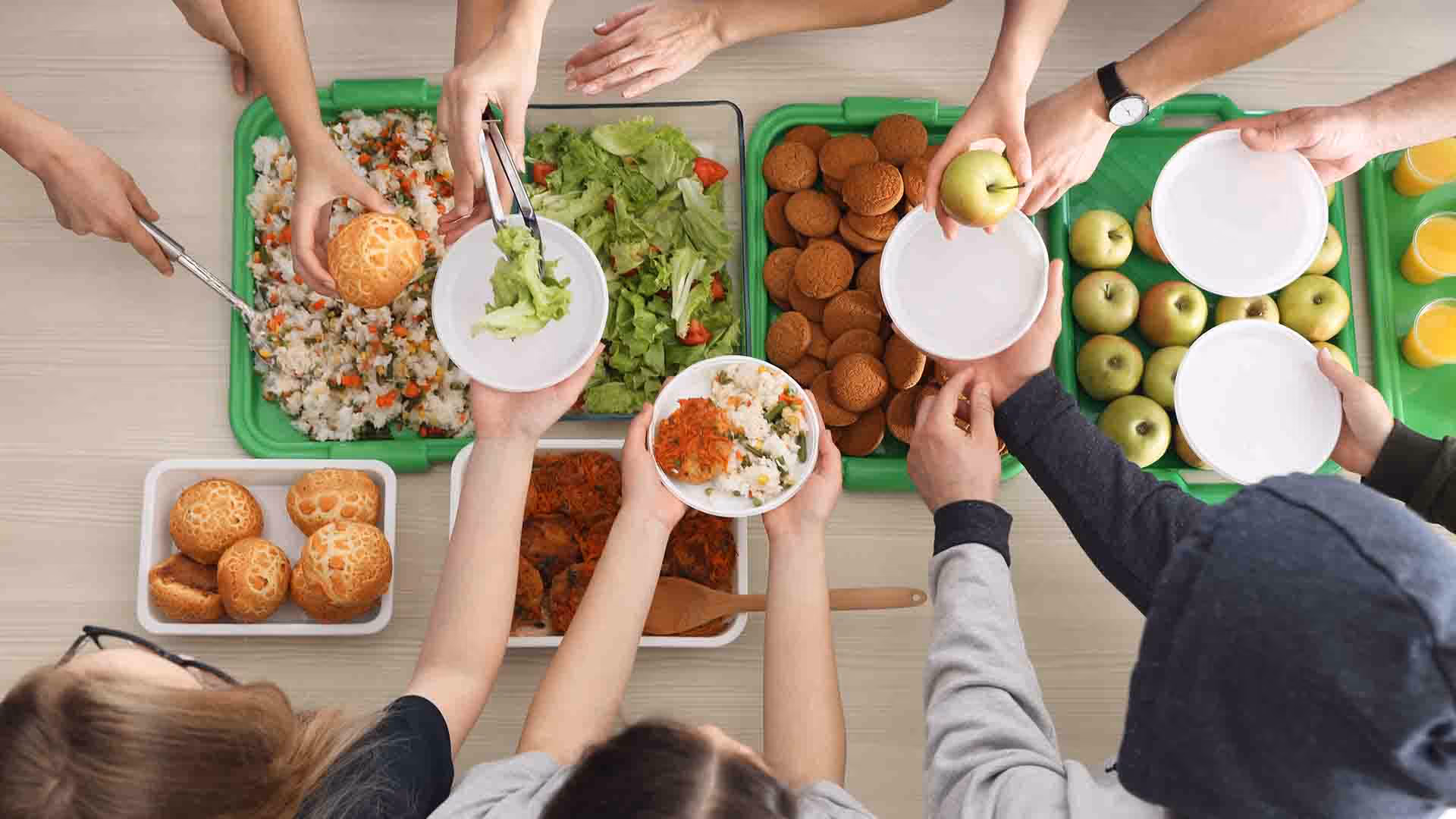 Overhead view of several people's hands serving healthy sustainable food and fruit onto white plates.