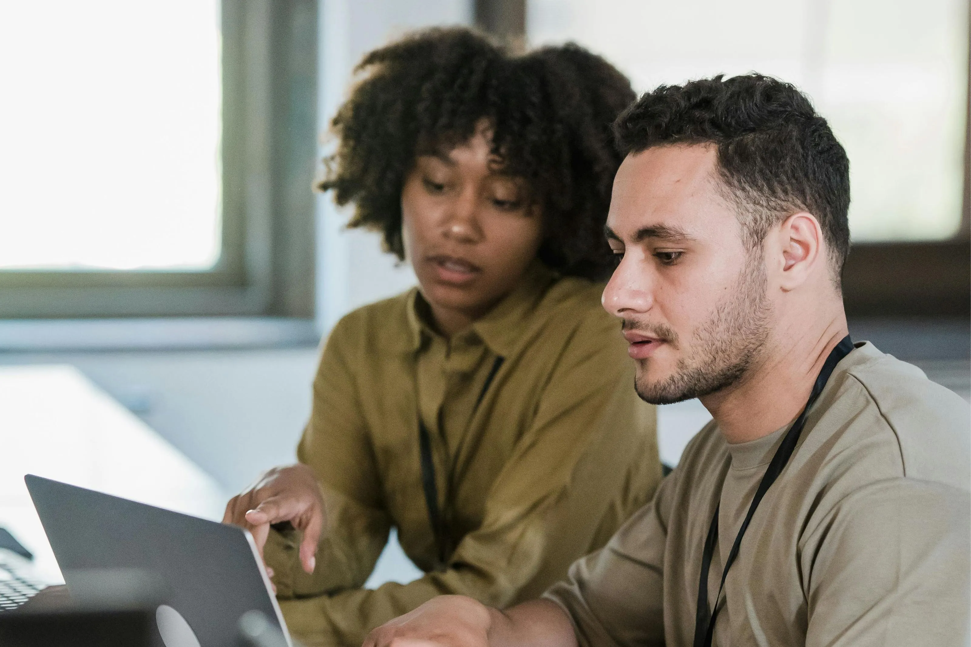 Two colleagues, a woman and a man, discussing work while looking at a laptop screen in an office.