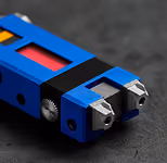 Close-up of a blue and black mechanical component with two metallic prongs on a dark surface.