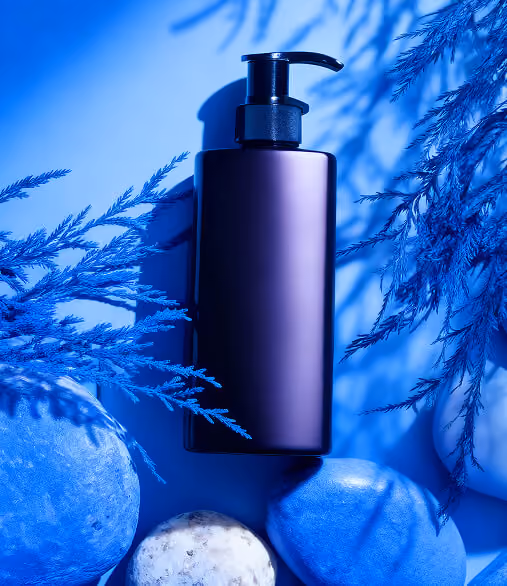 Purple pump bottle surrounded by blue-toned stones and foliage on a blue background.