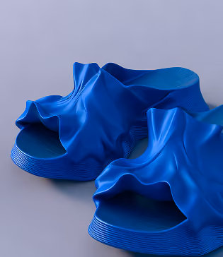 Pair of stylish blue slide sandals with ruffled fabric-like upper design on a gray background.