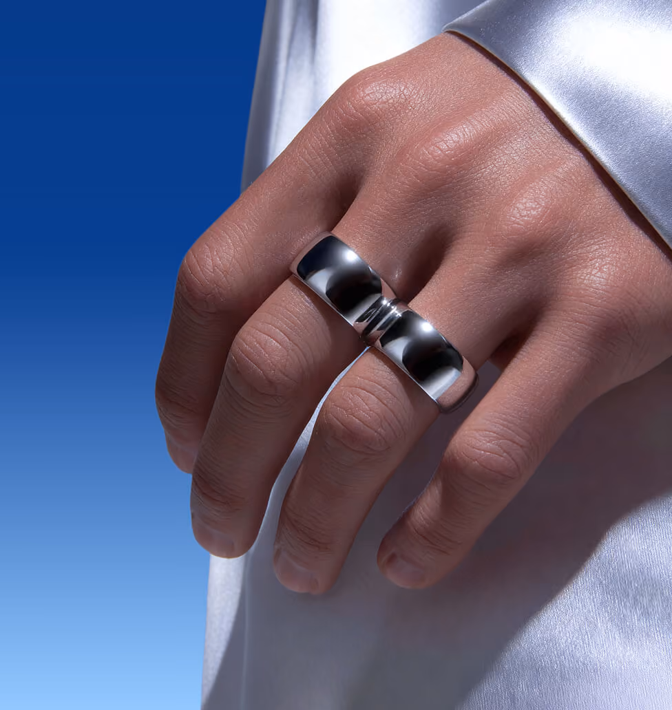Close-up of a hand wearing a sleek, reflective silver ring on the middle finger against a gradient blue background.