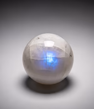 Transparent spherical crystal ball with a blue glow inside on a gray surface.