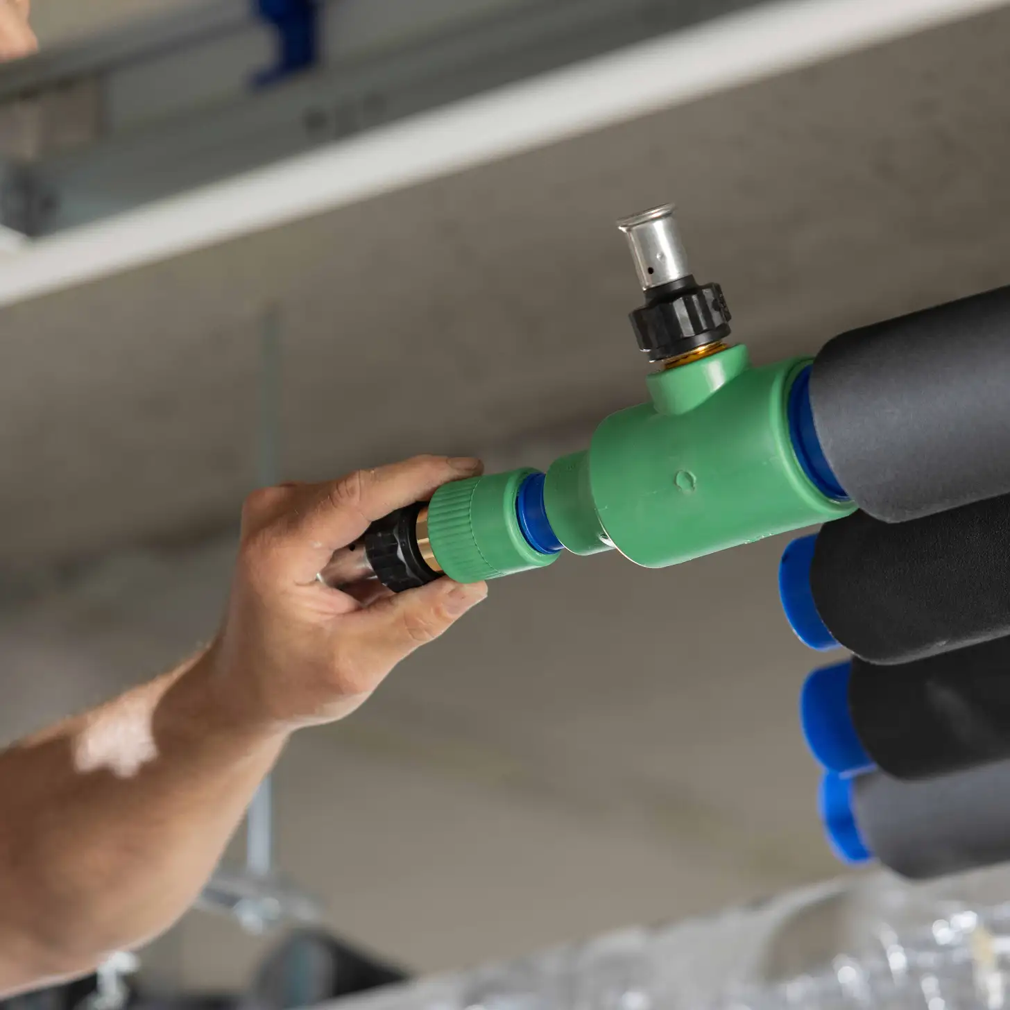 Hand die een groene en blauwe pijp met isolatie bevestigt aan een metalen fitting aan het plafond.