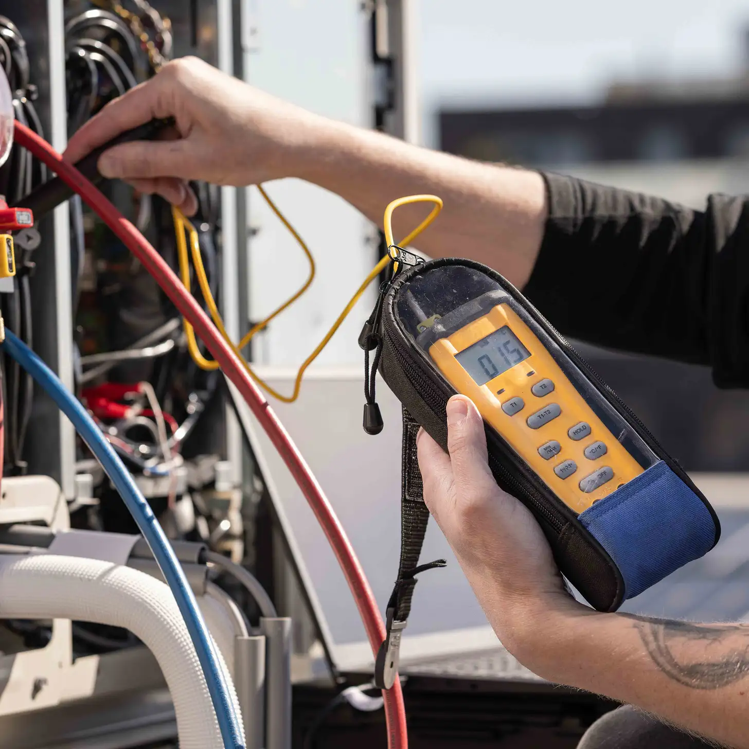 Technicus gebruikt een gele digitale meter om elektrische metingen te verrichten aan een apparaat met rode en blauwe kabels.