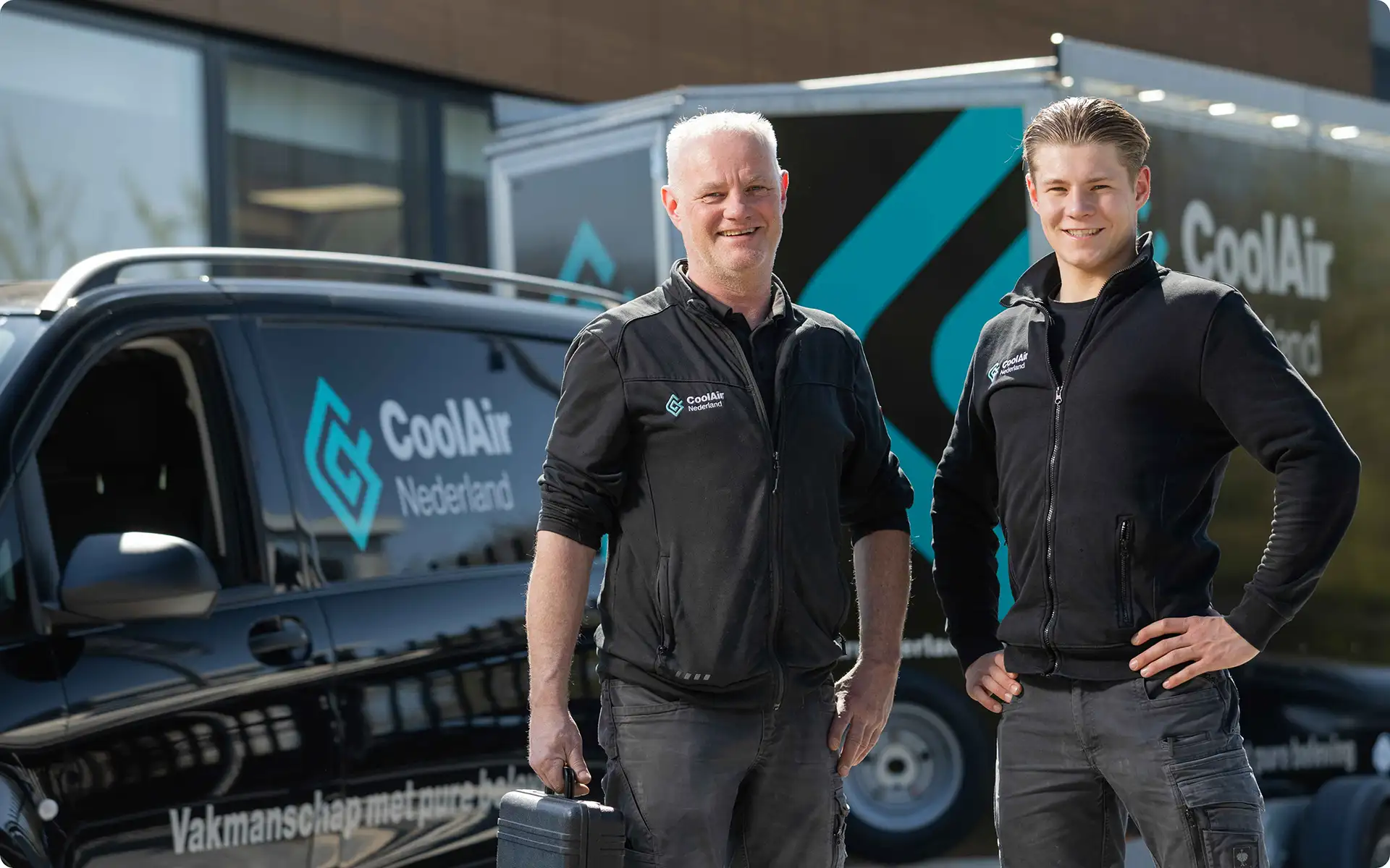 Twee mannen in zwarte jassen met logo's van CoolAir Nederland staan voor een bedrijfswagen en aanhangwagen met hetzelfde logo.