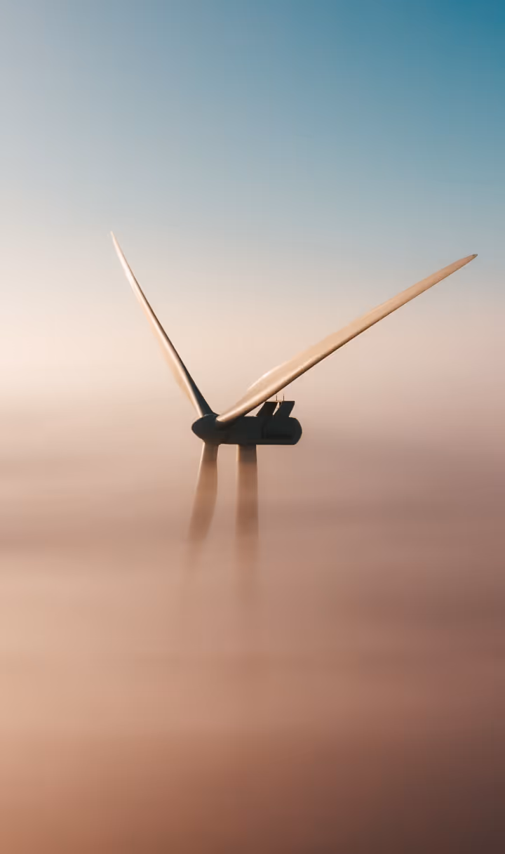Wind turbine blades protruding above dense fog under a clear blue sky.
