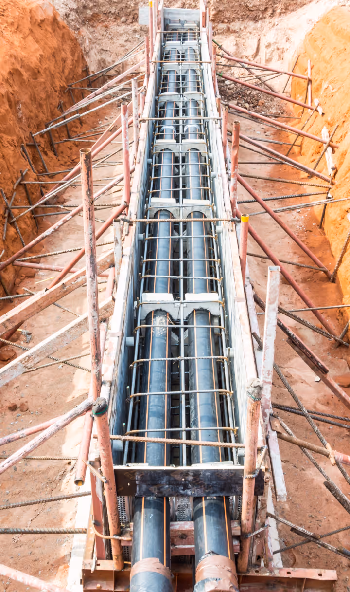 Construction site trench with reinforced steel framework holding large black pipes in place within the earth.