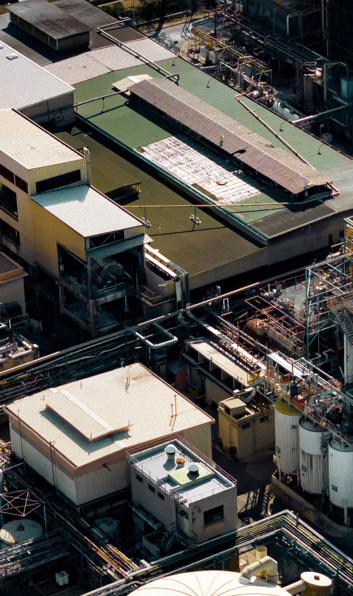Aerial view of an industrial complex with multiple buildings, pipelines, and storage tanks.