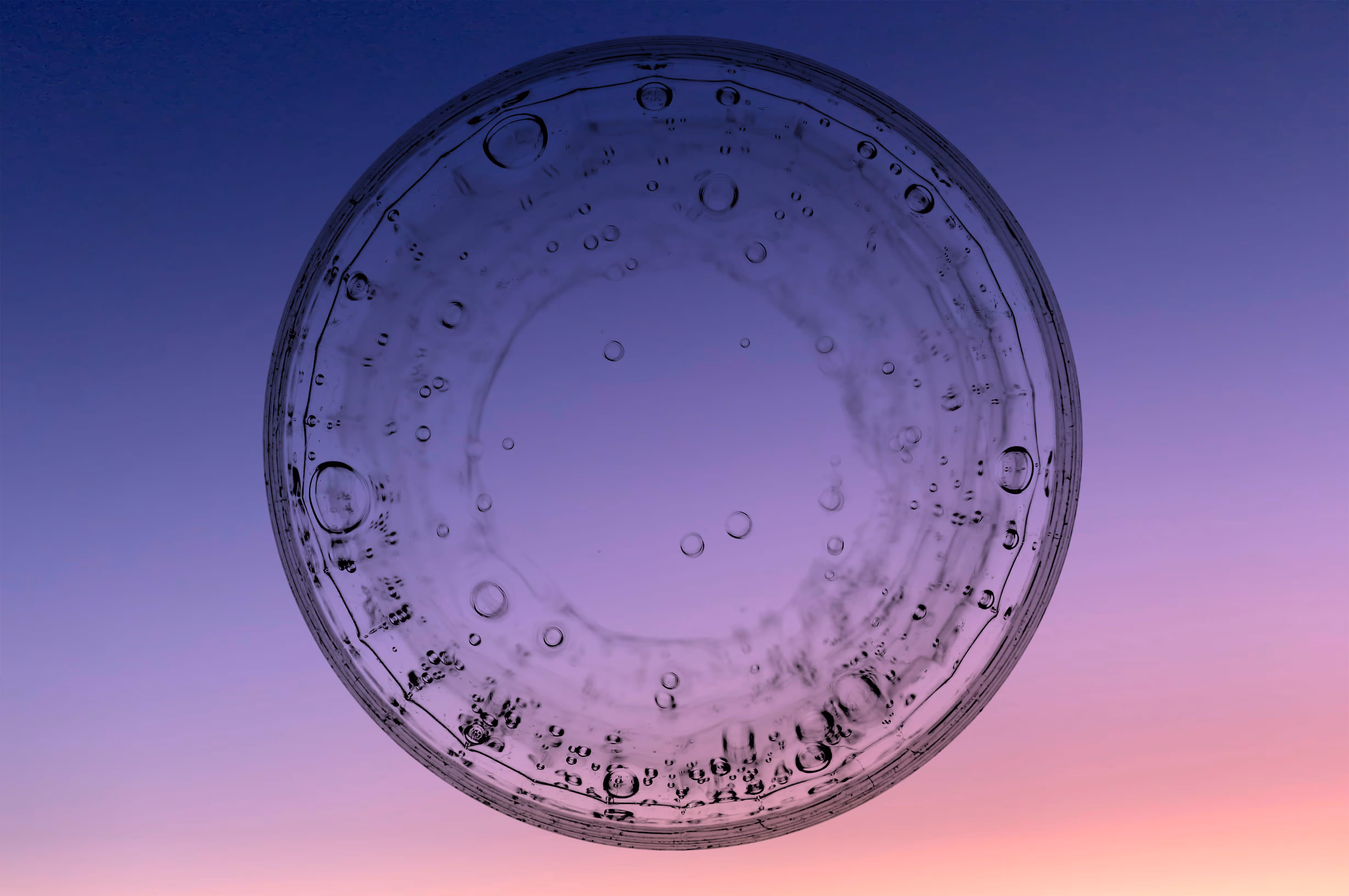 Close-up of a transparent circular object with water droplets against a gradient purple and pink background.