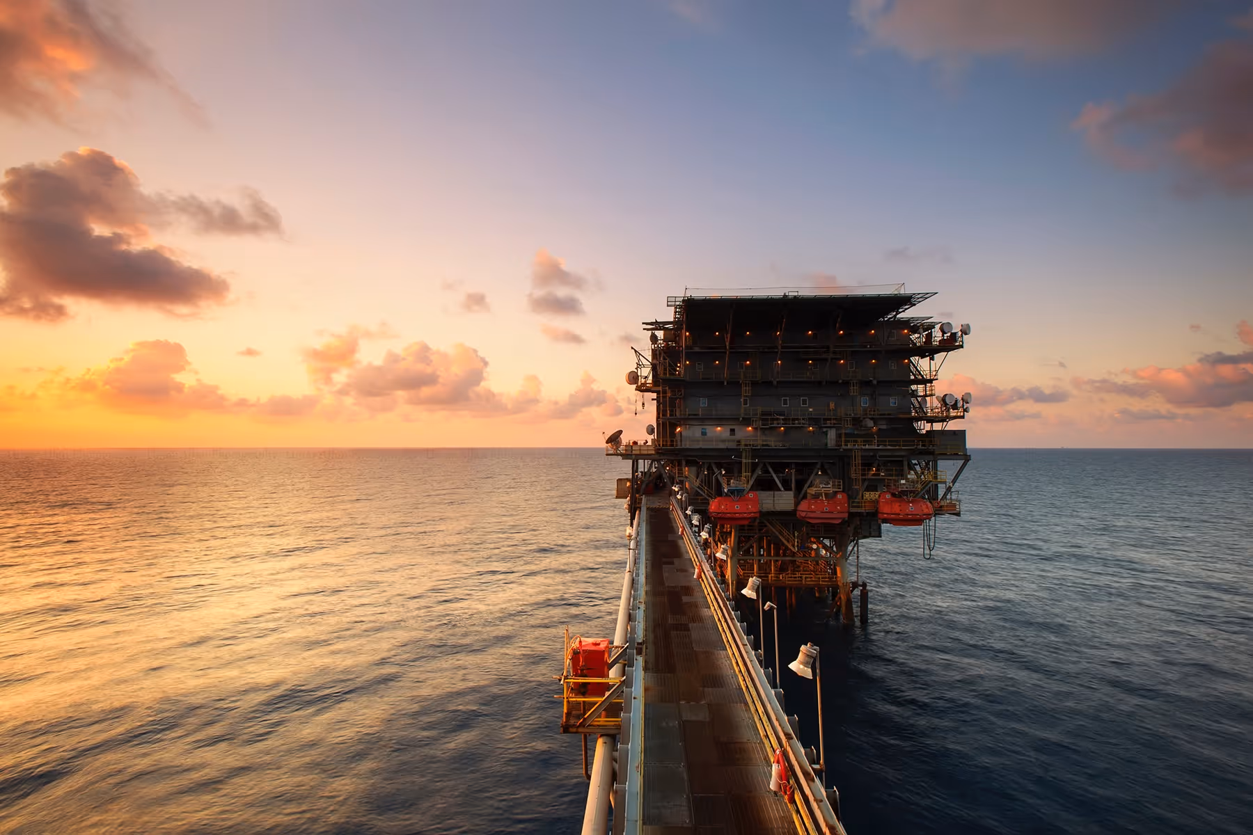 Offshore oil platform at sunset over calm sea with partly cloudy sky.
