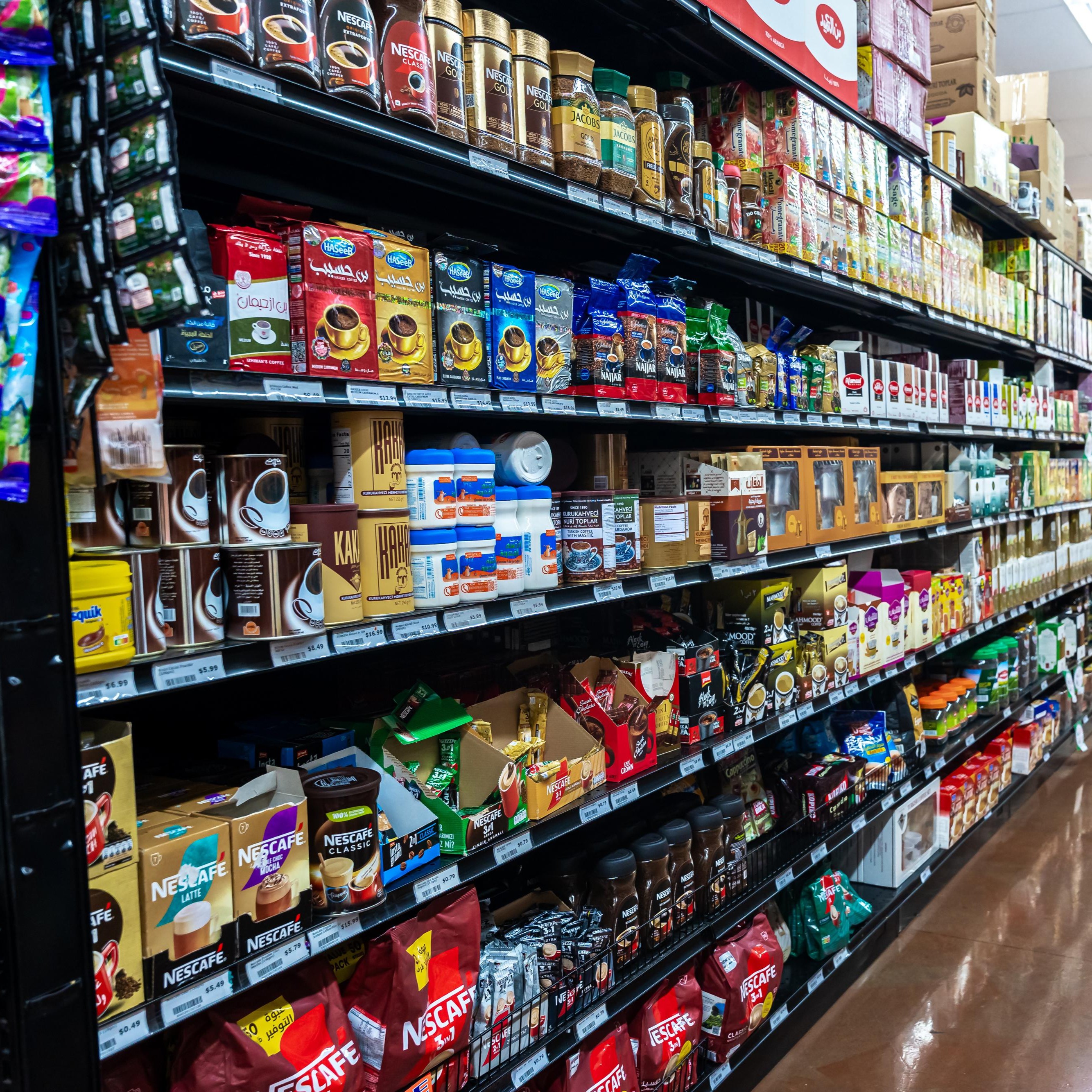 Supermarket aisle shelves stocked with various coffee brands and instant coffee products, including Nescafe and other international labels.