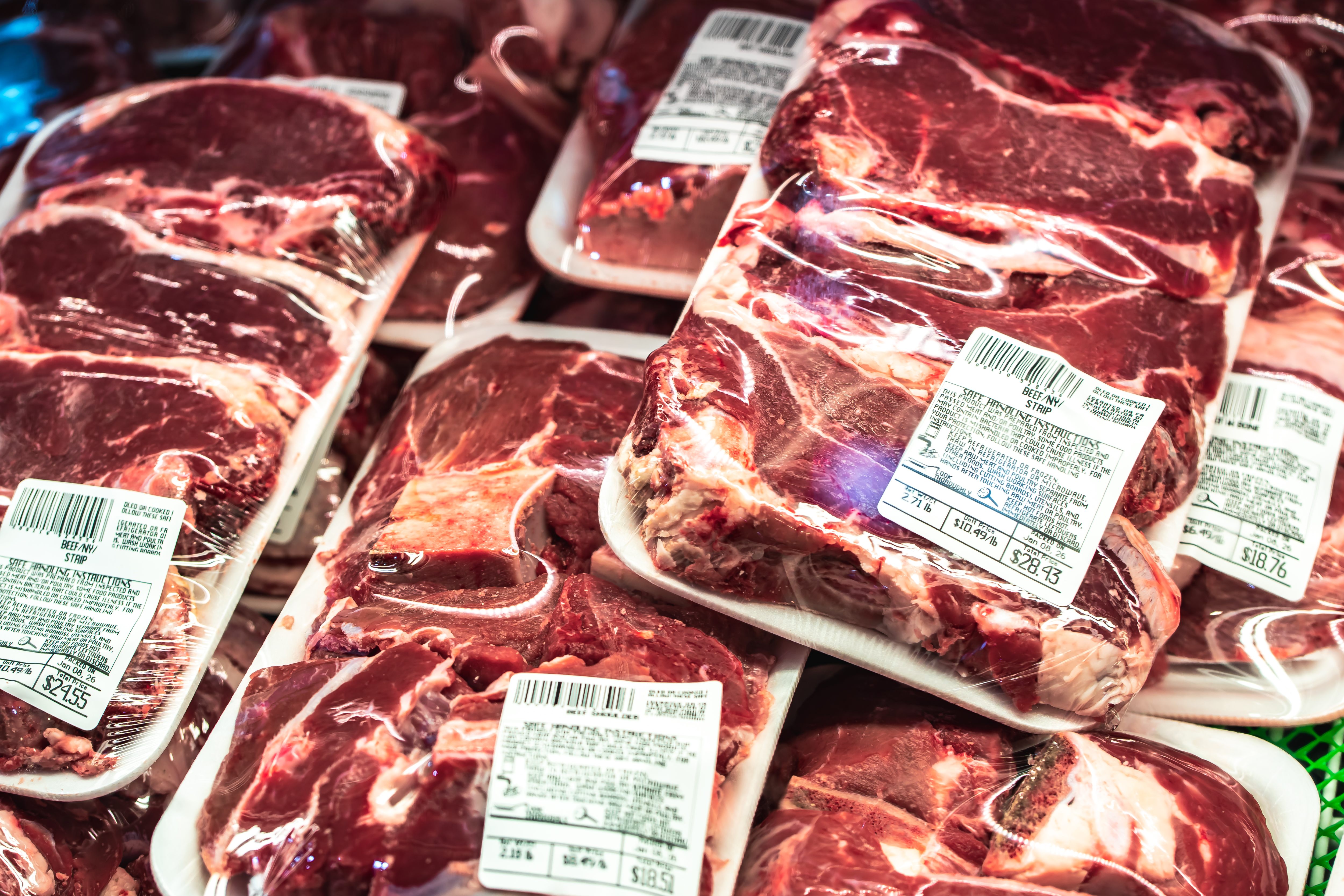 Raw T-bone steak with fresh rosemary sprigs on a dark textured surface.