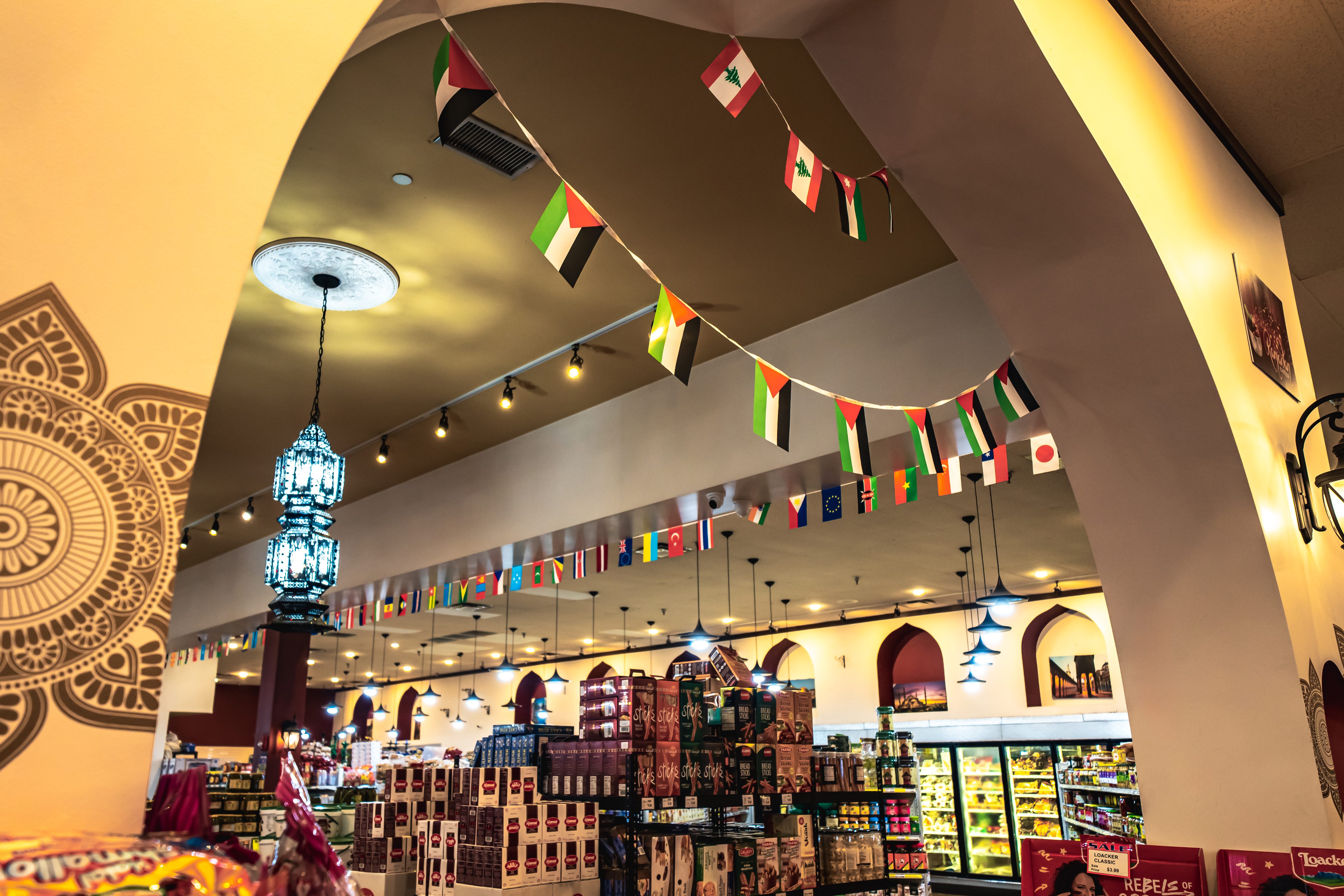 Interior of a grocery store with shelves stocked with various products under hanging lights and numerous international flags.