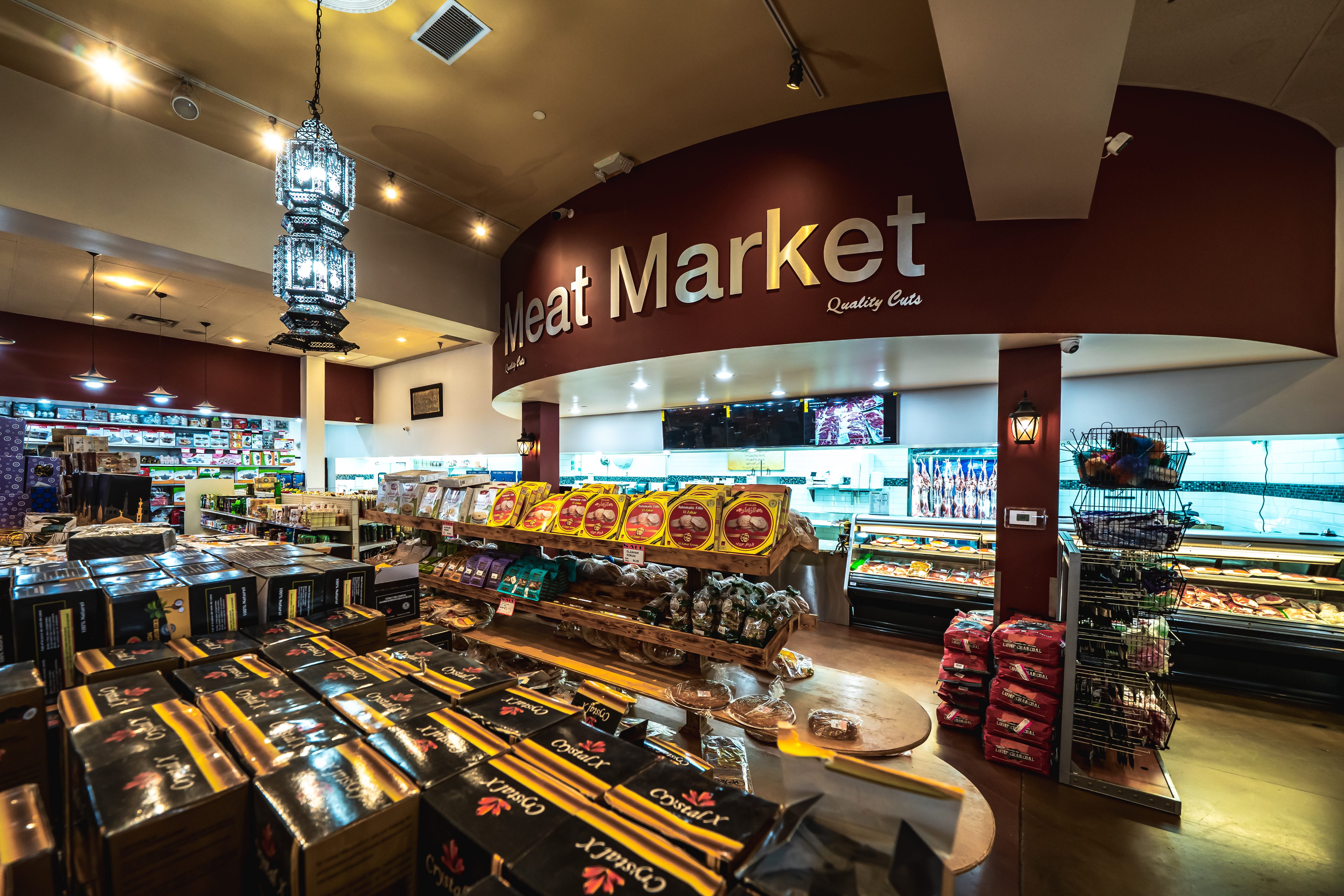 Interior of a meat market with packaged goods, hanging meat in a refrigerated display, and a sign reading 'Meat Market Quality Cuts.'