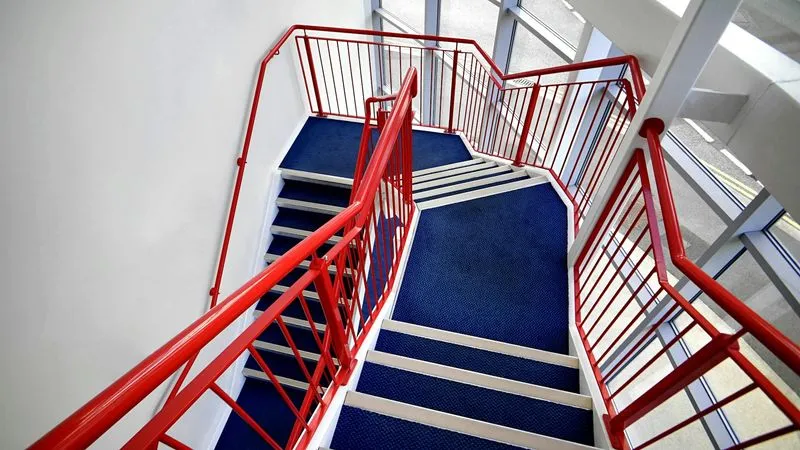 A red and blue stair case next to a window.