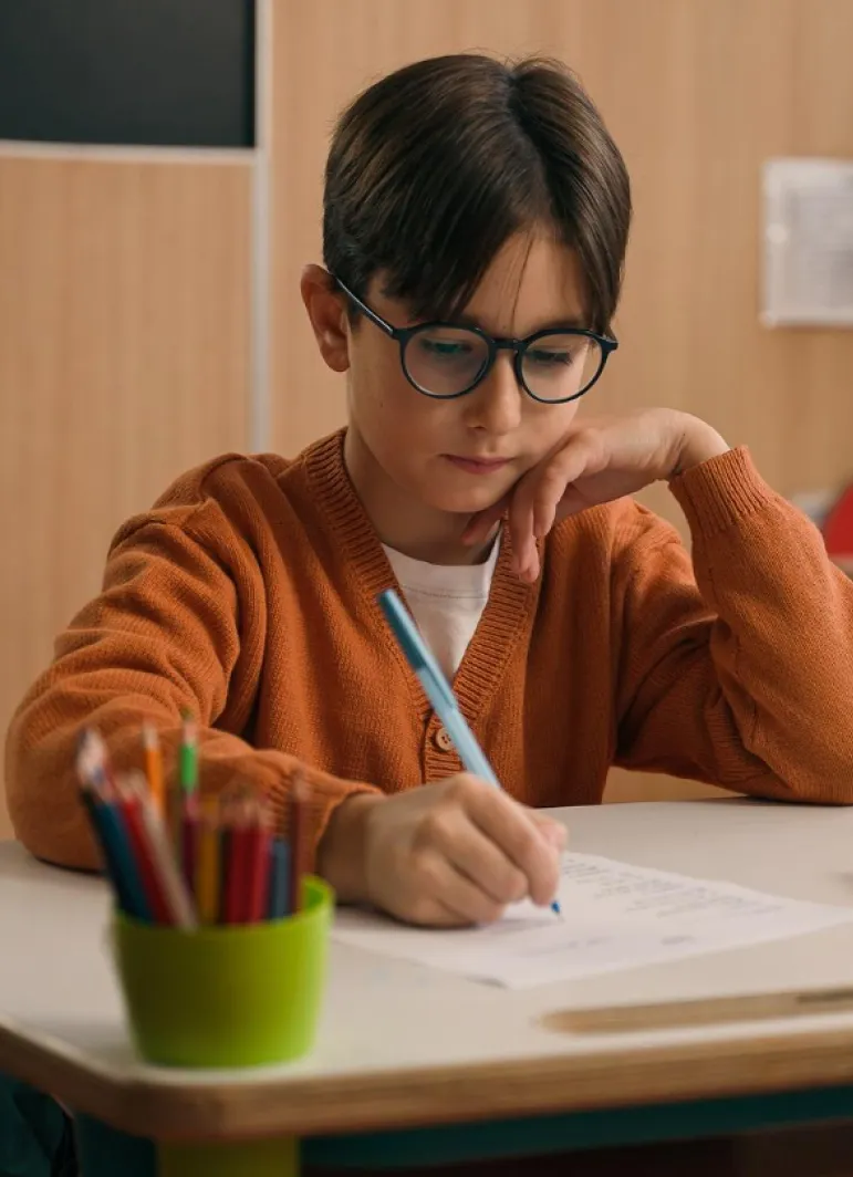 A young boy sitting at a desk writing on a piece of paper.
