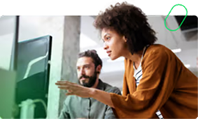 Woman pointing at a desktop computer screen while a man looks on attentively in a modern office.