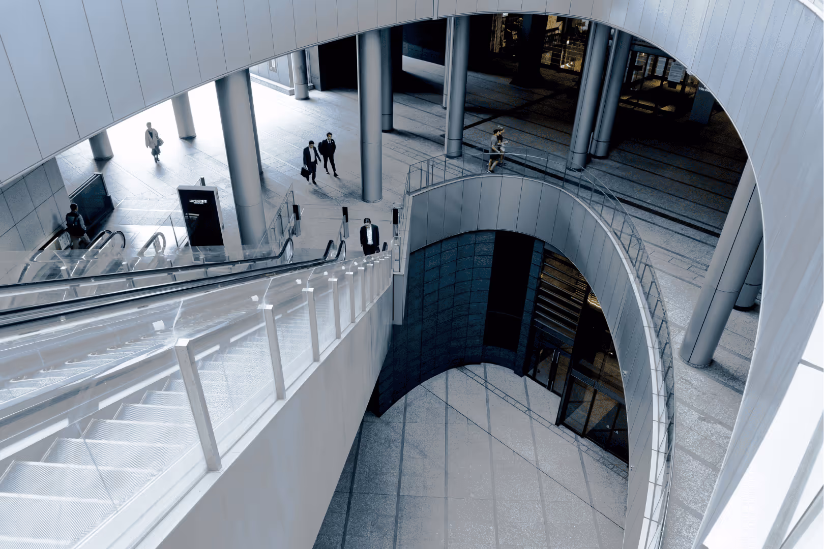 Modern architectural interior with spiral balcony, escalator, and people walking in a spacious corridor with large pillars.