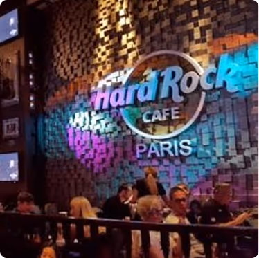 Intérieur animé du Hard Rock Café Paris avec personnes assises et logo lumineux sur un mur texturé.