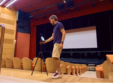 Un homme réglant un appareil photo sur un trépied dans une salle de théâtre vide avec des sièges orange.