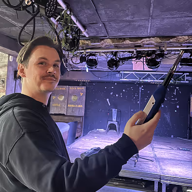 Un homme souriant tenant un allume-feu électrique dans une salle de spectacle avec scène et éclairage en hauteur.