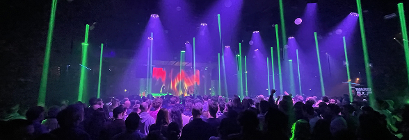 Foule dans une salle de concert avec éclairage violet et lumières vertes verticales.