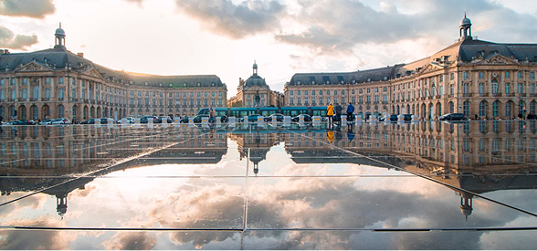 Place de la Bourse à Bordeaux avec son miroir d'eau reflétant les bâtiments du XVIIIe siècle sous un ciel nuageux.