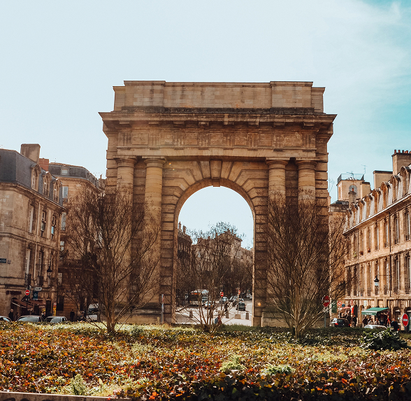 Grande arche en pierre au centre d'un rond-point, entourée de bâtiments historiques et de végétation à Lyon.