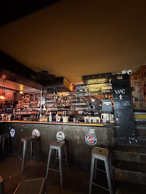 Comptoir d'un bar en intérieur avec des chaises hautes et un panneau qui indique les consommation et le WC 