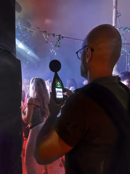 un acousticien tient un sonometre à proximité d'une enceinte dans une foule