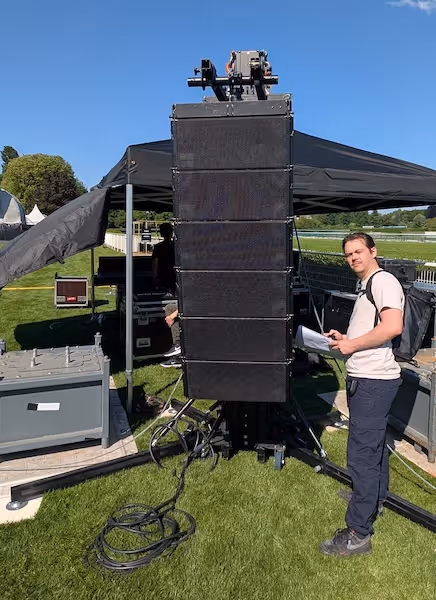 une personne se tient devant une grappe d'enceintes posée au sol