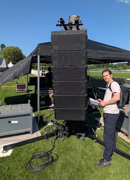 une personne se tient devant une grappe d'enceintes posée au sol