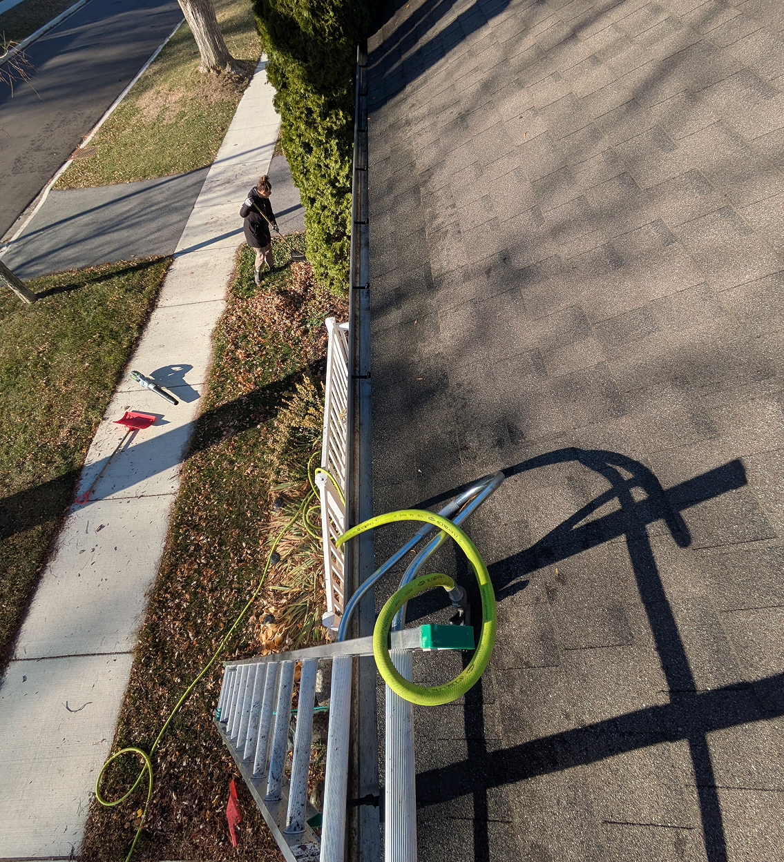 Worker clearing debris from residential gutter system using a scoop.