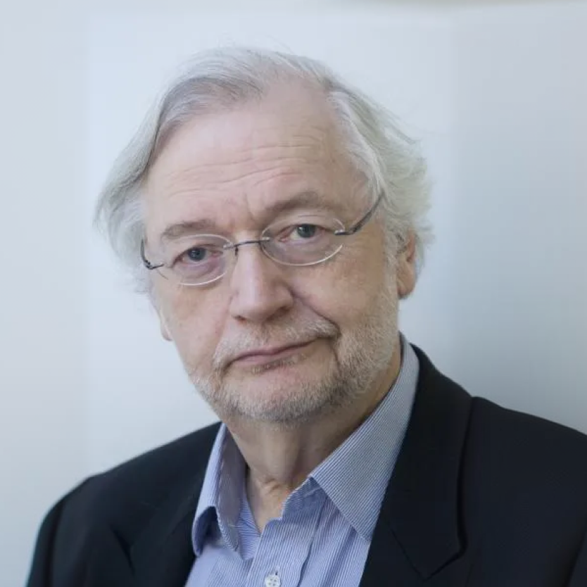 Man with glasses and beard speaking at a podium with a microphone in a lecture hall.
