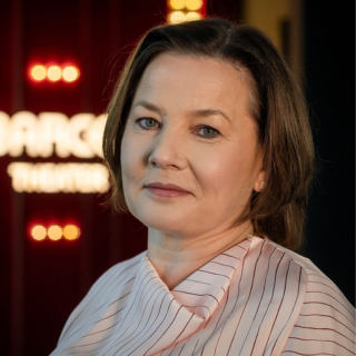 Man with glasses and beard speaking at a podium with a microphone in a lecture hall.