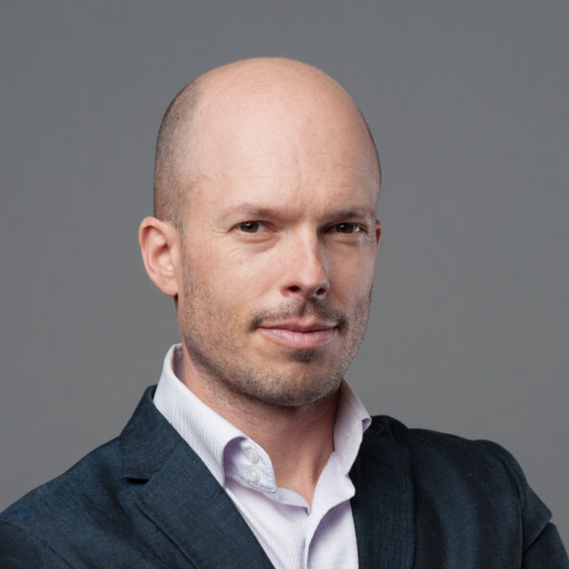 Man with glasses and beard speaking at a podium with a microphone in a lecture hall.