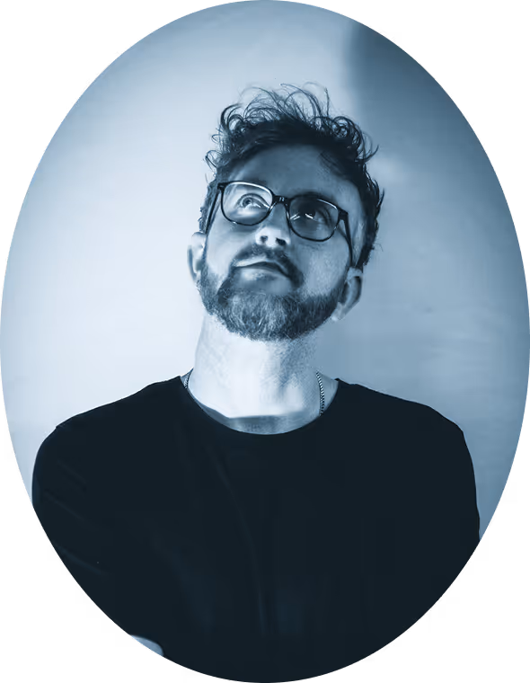 Bearded man with glasses looking upward wearing a dark shirt against a light background.