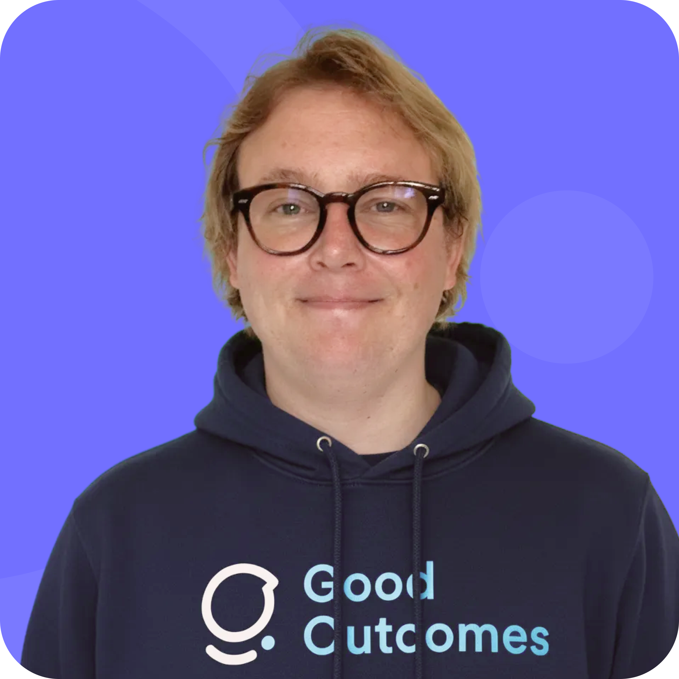Person with short blond hair and glasses wearing a navy hoodie with the words 'Good Outcomes' on a blue background.
