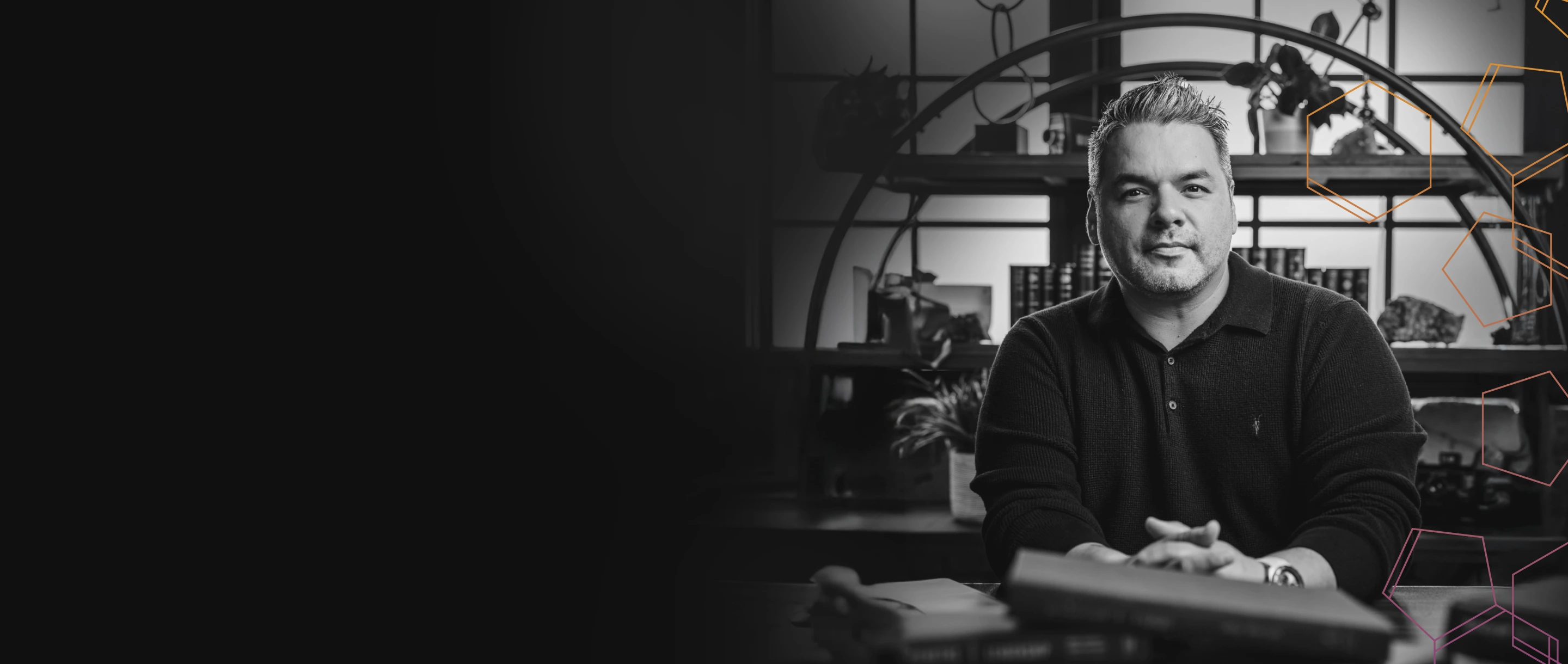 Ricky Ratcliff wearing a dark sweater sitting at a desk with books and a bookshelf in the background.